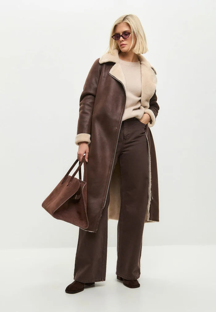 A stylish woman wearing a brown faux fur coat that can be reversed to a shearling texture, a fashionable and versatile long shearling jacket for women.