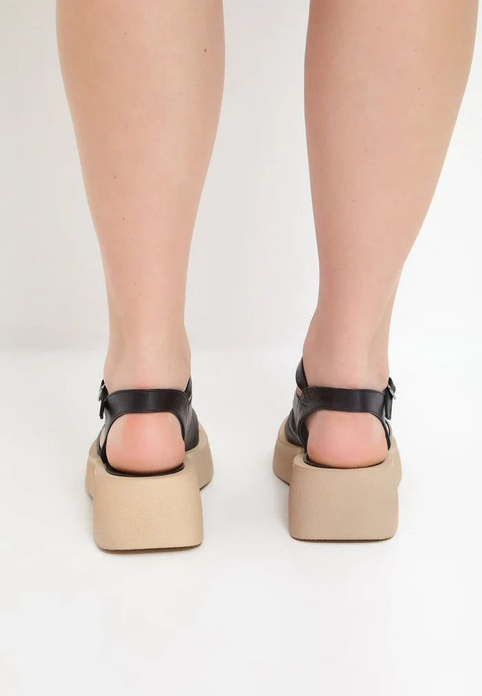 A woman's feet wearing stylish black platform sandals, the perfect mix of casual and comfortable footwear for any occasion.