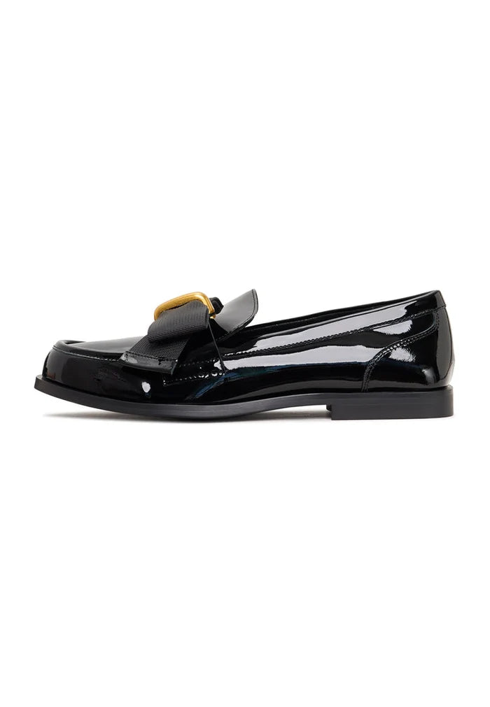 A pair of elegant black patent loafers with a stunning gold bow detail, inspired by Dorothy's iconic shoes, perfect for women's fashion.
