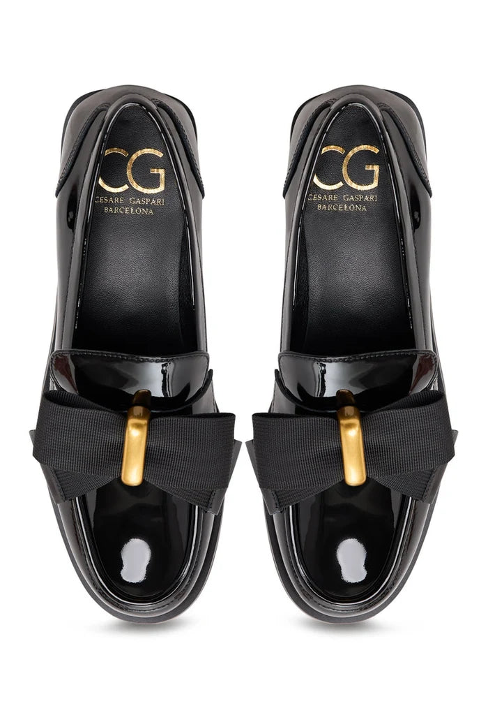 A pair of elegant patent black women's shoes with a gold bow detail, inspired by Dorothy's iconic style.