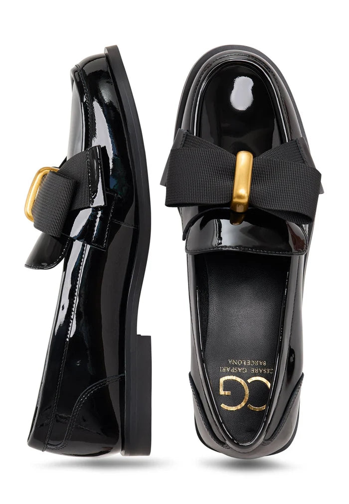 A pair of elegant patent black women's loafers with a gold bow inspired by Dorothy's iconic style.