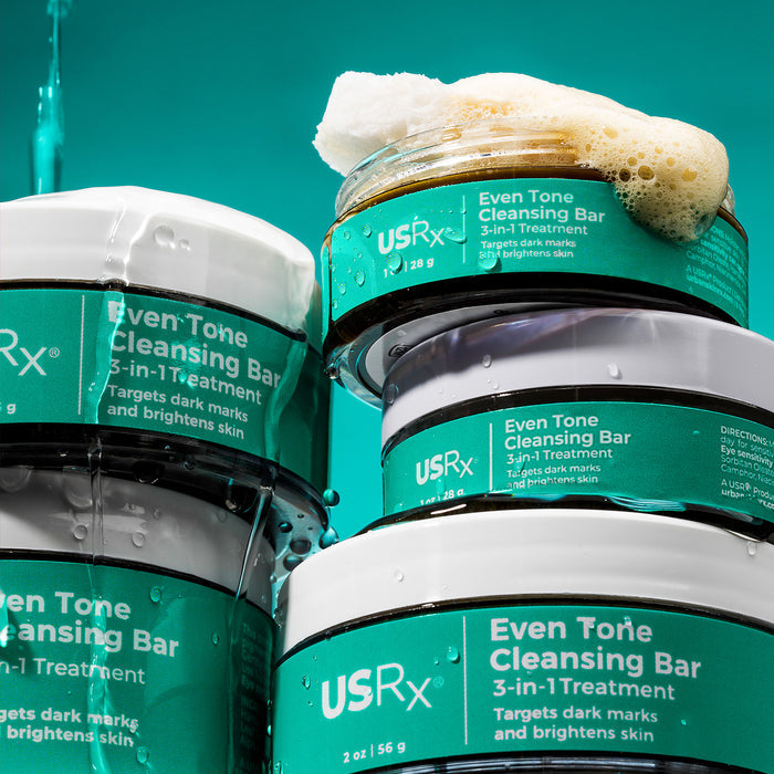 Multiple jars of USRx Even Tone Cleansing Bar on a green background, with lather coming out of open jar
