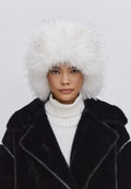 Woman wearing a stylish winter fashion hat, the Irina faux fur hat in black and white, paired with a black coat and white turtleneck.