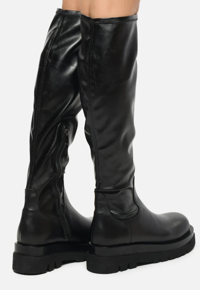 A woman wearing trendy leather lug knee-high boots, a stylish choice for any fashion-forward outfit.