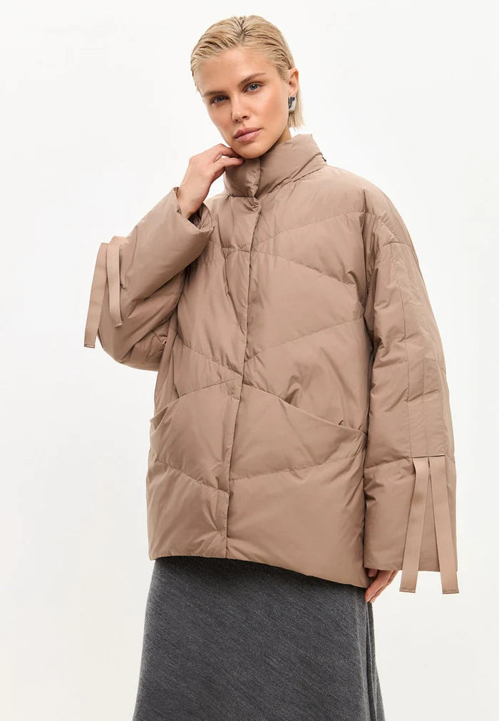 A woman wearing an oversized quilted beige puffer jacket, perfect for winter outerwear and a fashionable statement piece.