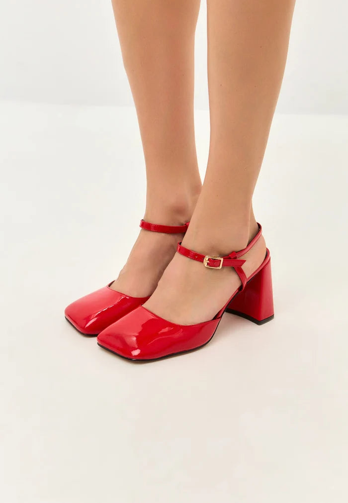 A close-up image of red patent block heel pumps, showcasing the sleek design and glossy finish of these stylish patent leather shoes.