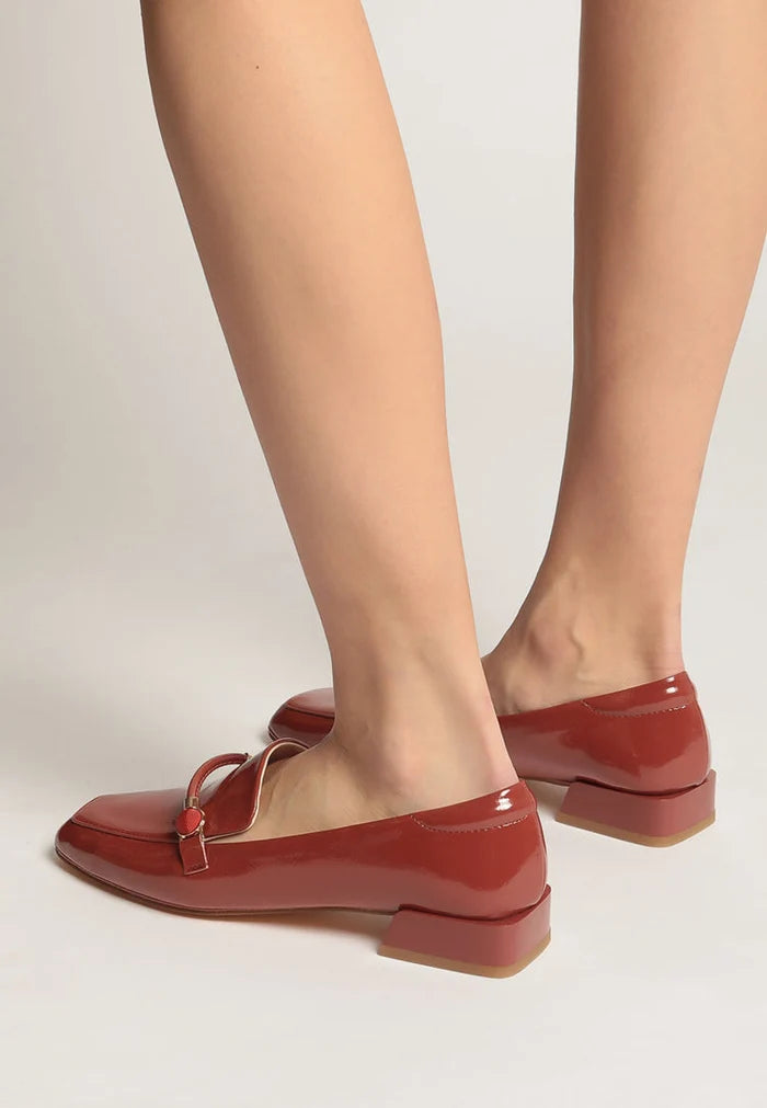 A stylish pair of patent leather loafers with metallic accents in an eye-catching orange color, perfect for slipping on with any outfit. Fashionable leather slip-on shoes for a trendy look.