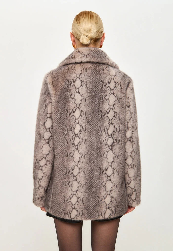 A fashionable woman wearing a beige faux fur Niuvis coat with snake print trim, a stylish outerwear choice for trendy winter fashion.