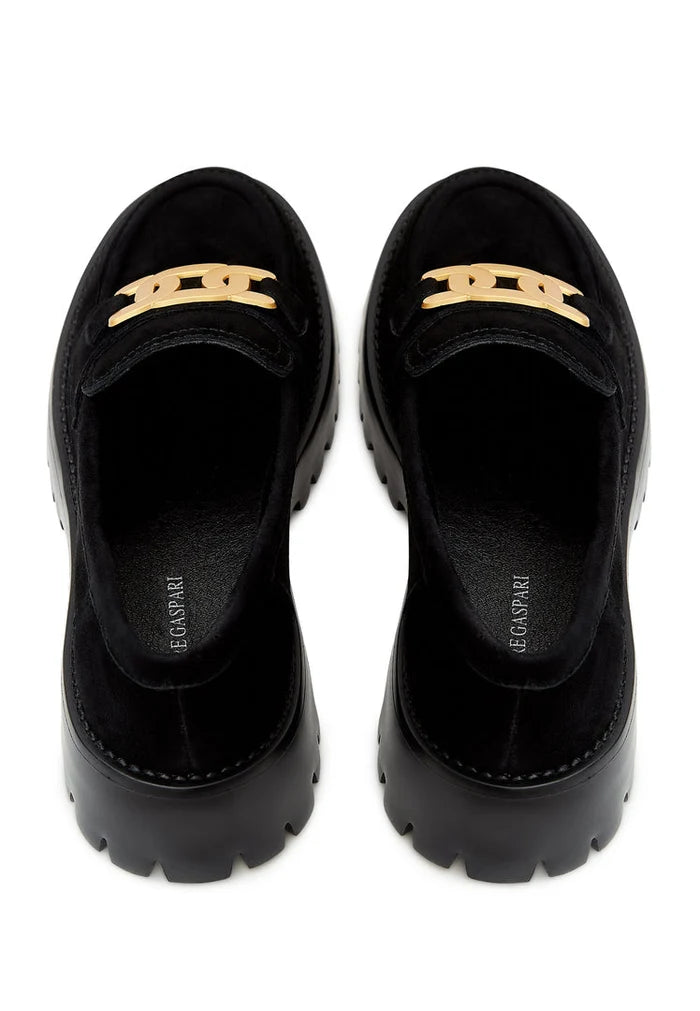 A fashionable pair of chunky black loafers with a golden chain detail, crafted from suede material, showcasing stylish footwear.